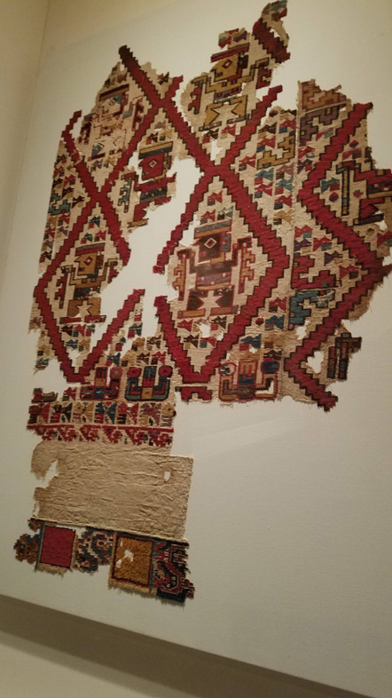 A Mochican textile with birds, snakes and a human carrying canes.